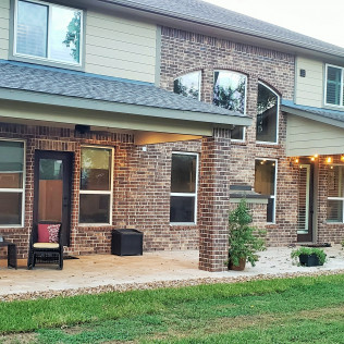 Two-story brick house with a covered patio, windows, and green lawn.