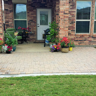 Brick patio with door, windows, plants, and green lawn.