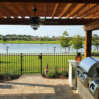 Patio with pergola, outdoor kitchen, view of lake, fence, and trees.