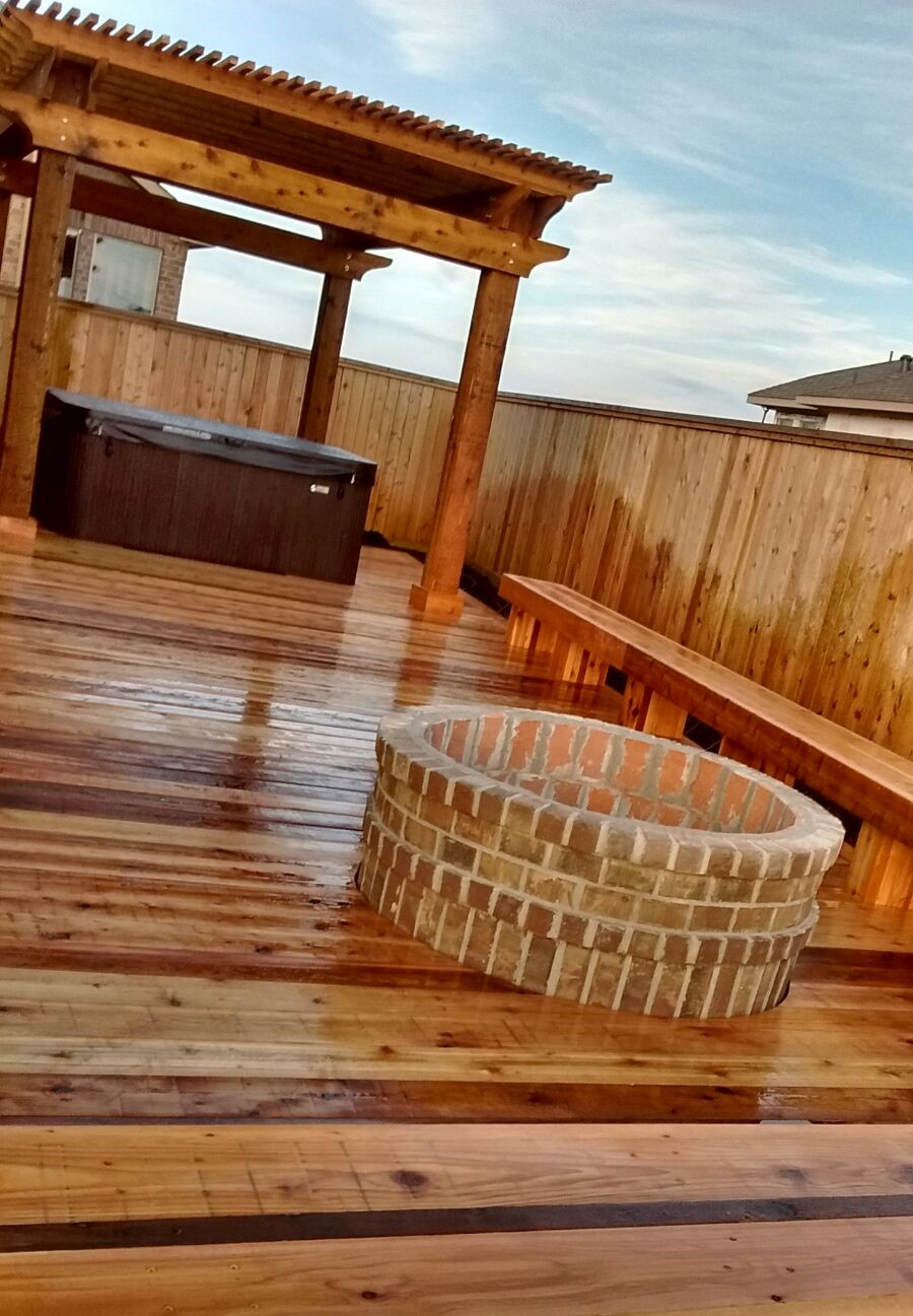 Wooden deck with hot tub, fire pit, and pergola against a wooden fence.