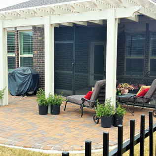 Patio with brick pavers, lounge chairs, potted plants, and a grill under a white pergola.