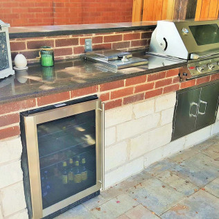 Outdoor kitchen with brick facade, granite countertop, grill, cooler, and cabinet.