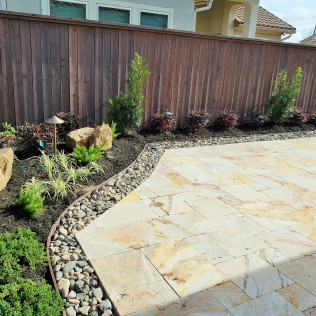 Stone patio with a border of rocks and landscaping against a wooden fence.