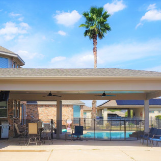 Backyard patio with pool, palm tree, and houses under a bright blue sky.
