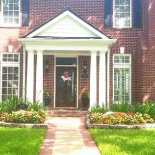 Red brick house with white columns, a front door, and a brick walkway leading to it.