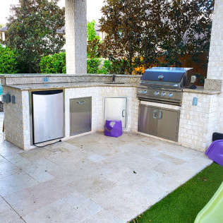 Outdoor kitchen with a grill, refrigerator, and storage in a tiled space.