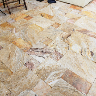 Tan and gold stone tile floor in a herringbone pattern with a mix of colors and textures.