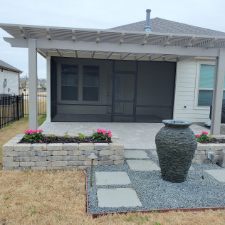Patio with pergola, screening, and a raised flower bed. Large water feature in the foreground.