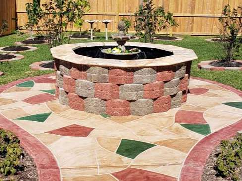 Octagonal brick fountain in a yard with a colorful paved pathway.