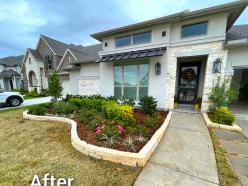Front yard landscaping of a house with stone border, mulch, and colorful plants.