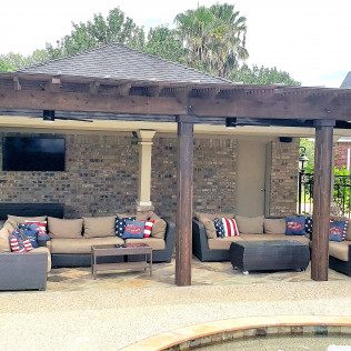 Outdoor patio with seating under a pergola, brick wall, and a pool.