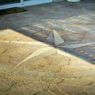 Flagstone patio with a star-shaped inlay, shaded by a latticework.