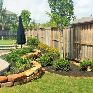 Backyard landscaping with stone retaining walls, plants, and wooden fence.