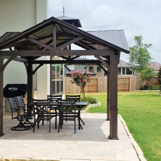 Gazebo with table and chairs on a patio, overlooking a backyard with a fence.