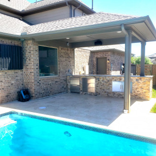 Backyard patio with pool, outdoor kitchen, and covered seating area, brick and stone construction.