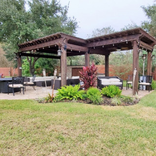 Outdoor patio with dark wood pergola, seating, landscaping and fire pit.