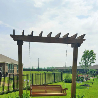 Wooden swing under a pergola in a backyard.