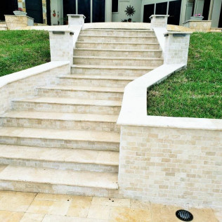 Stone steps leading up to a house, flanked by brick walls and green grass.