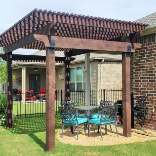 Wooden pergola over outdoor seating area in a backyard. Brown beams, blue chairs, patio.