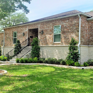 Brick house with black railings, green lawn, and shrubbery.