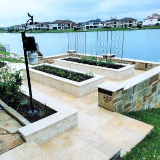 Raised garden beds next to a lake, with stone walls and a decorative trellis.