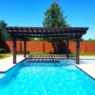 Pool with pergola, brick wall background, bright blue water and sky.