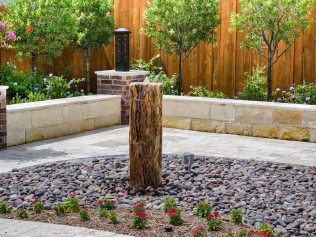 Landscaped yard with stone wall, gravel bed, and a tree trunk water feature.