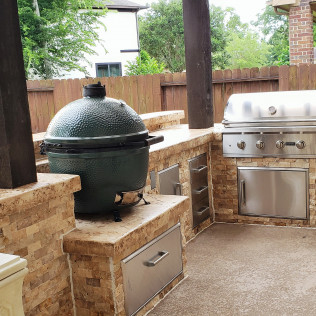 Outdoor kitchen with a Big Green Egg and stainless steel grill built into a stone structure.