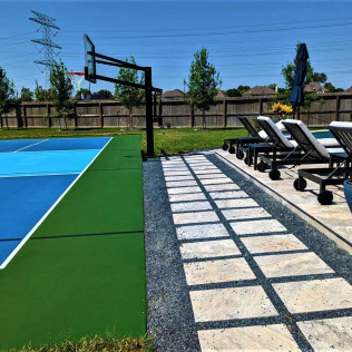 Outdoor basketball court with lounge chairs, a stone path, and a blue umbrella on a sunny day.