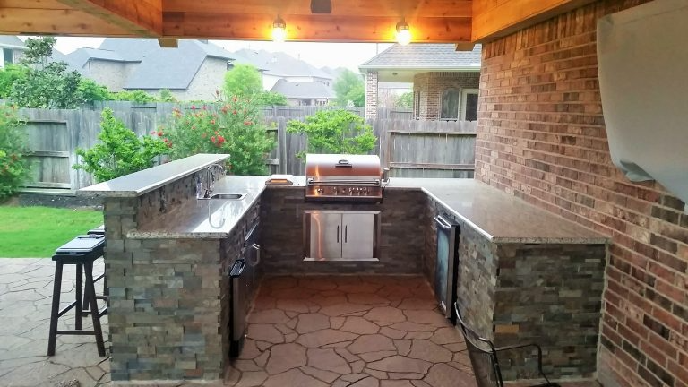 Outdoor kitchen with a brick wall, stone counters, and a built-in grill and refrigerator.