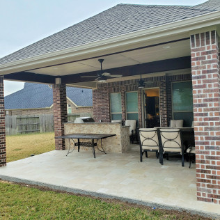 Covered patio with brick columns, seating, grill area, and ceiling fan.