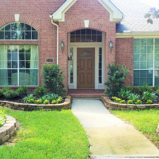 Brick home with landscaped front yard, pathway leading to a brown door with arched window above.