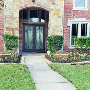 Stone and brick house entrance with a walkway, double doors, and manicured landscaping.