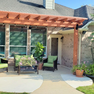 Patio with a wooden pergola, brick house, seating, and potted plants.