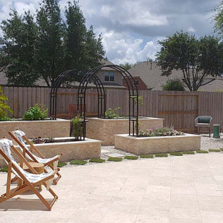 Backyard with three raised garden beds, arched trellises, wooden chairs, and a stone patio.