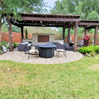 Outdoor patio with a pergola, stone fire pit, seating, and landscaping.