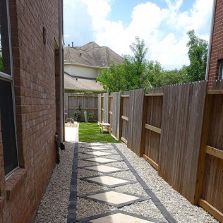 Path with diamond-shaped stones between a brick wall and a wooden fence; gravel on the sides.
