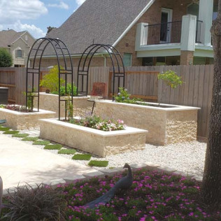 Backyard garden with stone planters, black arched trellises, and a peacock statue.