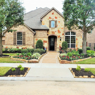 House with stone and brick facade, landscaped yard, and sidewalk.