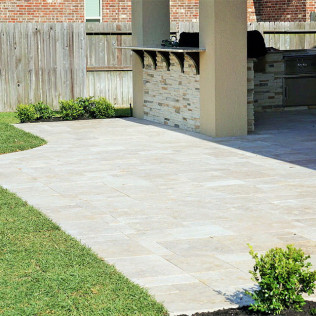 Patio with stone pavers, grass, outdoor kitchen with bar, and wooden fence.