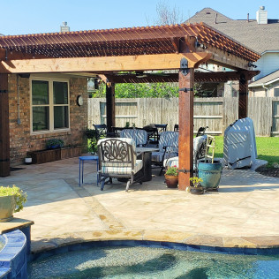 Outdoor patio with pergola over a seating area near a pool; sunny day.