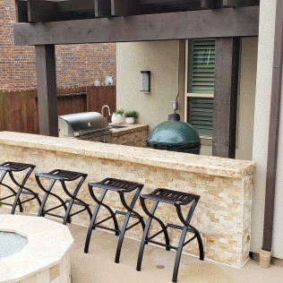 Outdoor kitchen with a grill, Big Green Egg, bar with stools, and pergola.