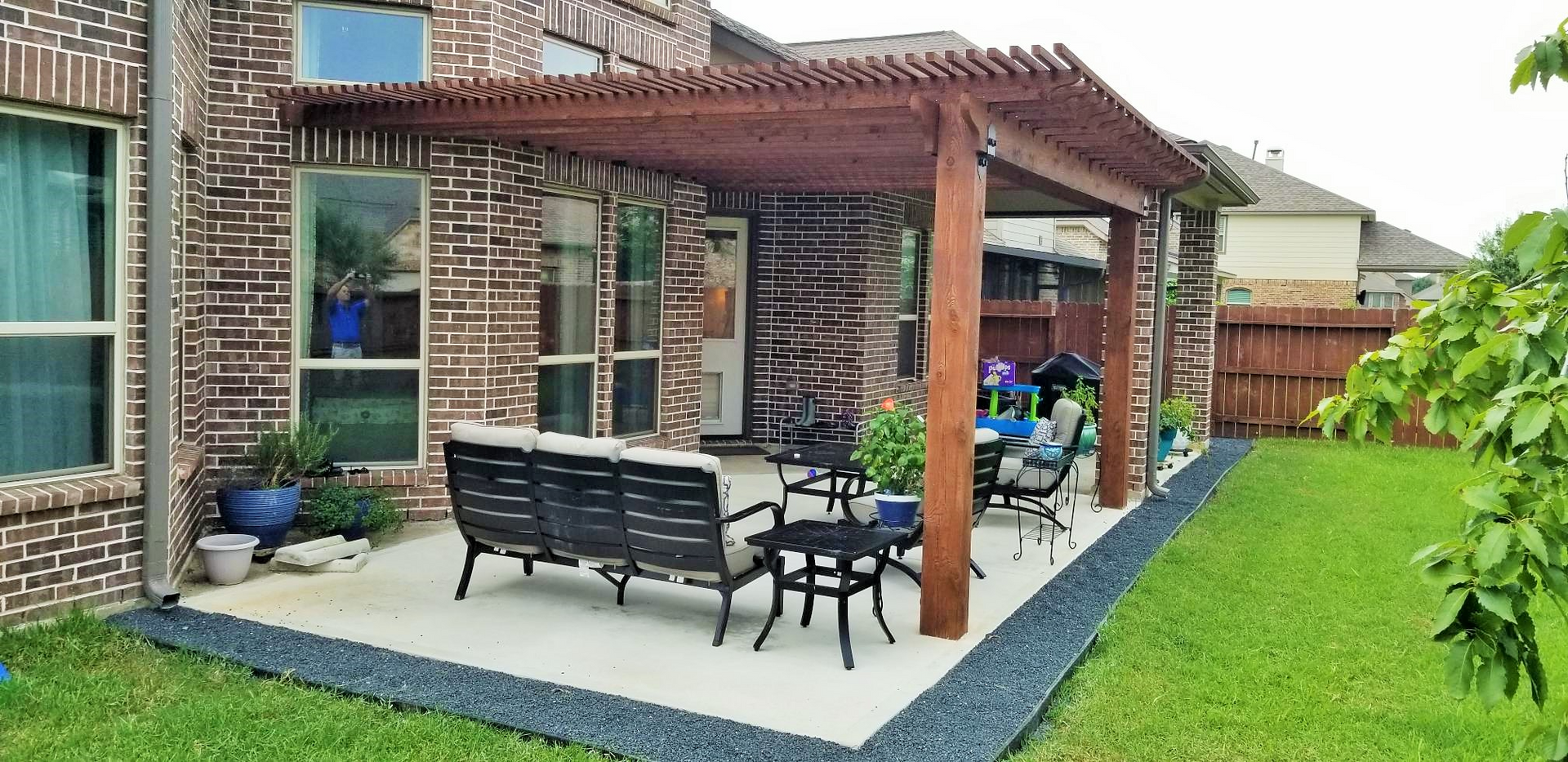 Backyard patio with a pergola, seating, and green lawn. Brick house.