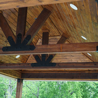 Wooden gazebo ceiling with dark beams, light wood panels, and black metal connectors.