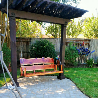 Wooden swing bench under a pergola in a backyard.