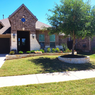 Suburban house with brick and stone facade, landscaped yard with circular tree bed and retaining wall.