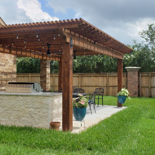 Outdoor patio with wooden pergola, built-in grill, seating area, and lush green grass.