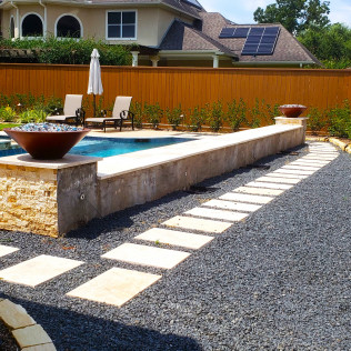 Stone pathway with pool, seating area, and fire bowls in a backyard with wooden fence.
