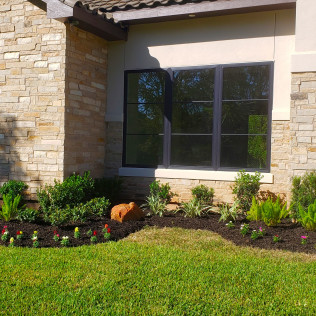 House exterior with window, landscaped flower bed, and lawn.