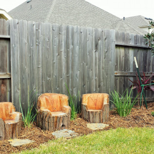 Three log chairs in a garden setting, against a weathered wooden fence.
